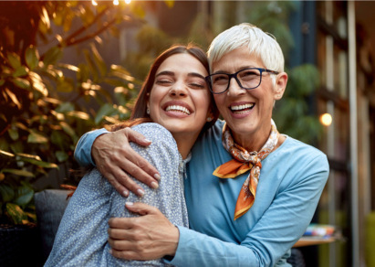 Older woman and younger woman embrace and smile 