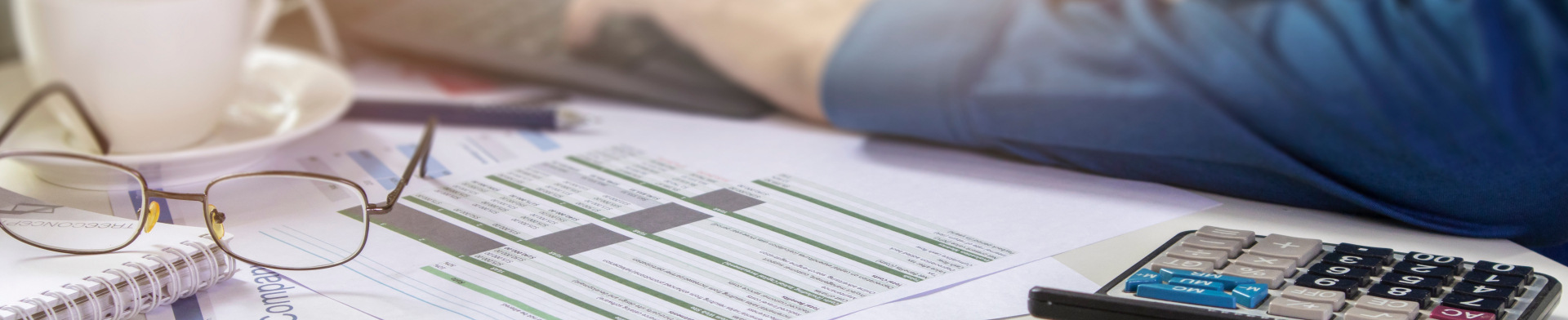 A coffee mug, glasses, tax documents, and a calculator set on a table.