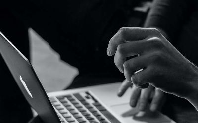 A black and white image of a person working on a laptop, symbolizing cybersecurity and digital protection