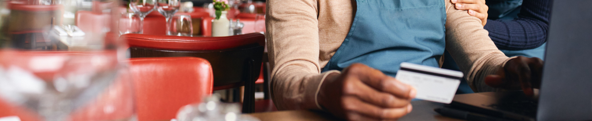 An employee using a business credit card sitting down in a chair in their restaurant.